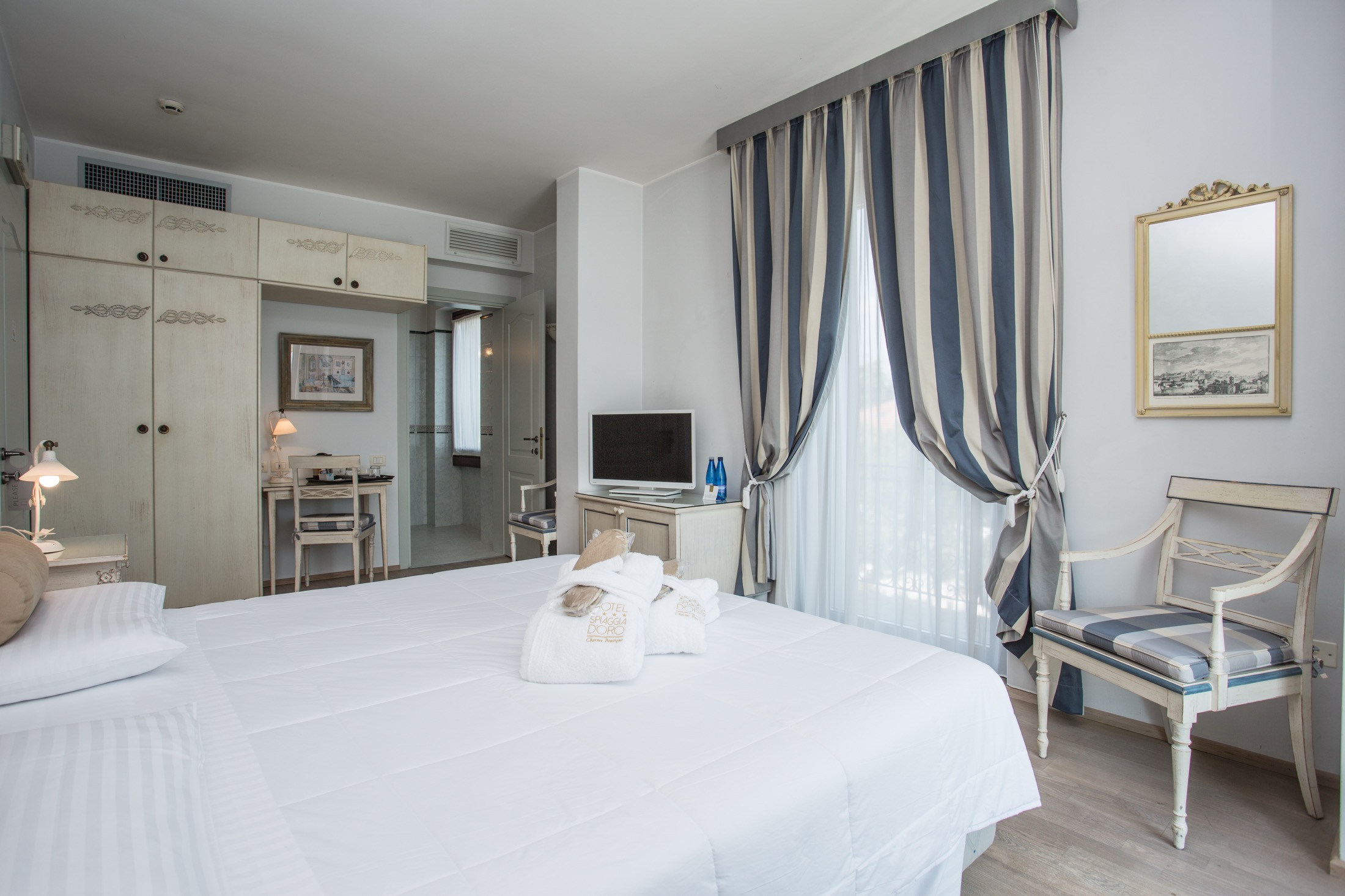 Zimmer mit natürlichen Tönen und warmen Holzböden sowie einem privaten Balkon, von dem aus ein angenehmer Seitenblick auf den See eröffnet wird, der das Wohnzimmer mit Licht, Ruhe und Landschaft begleitet.